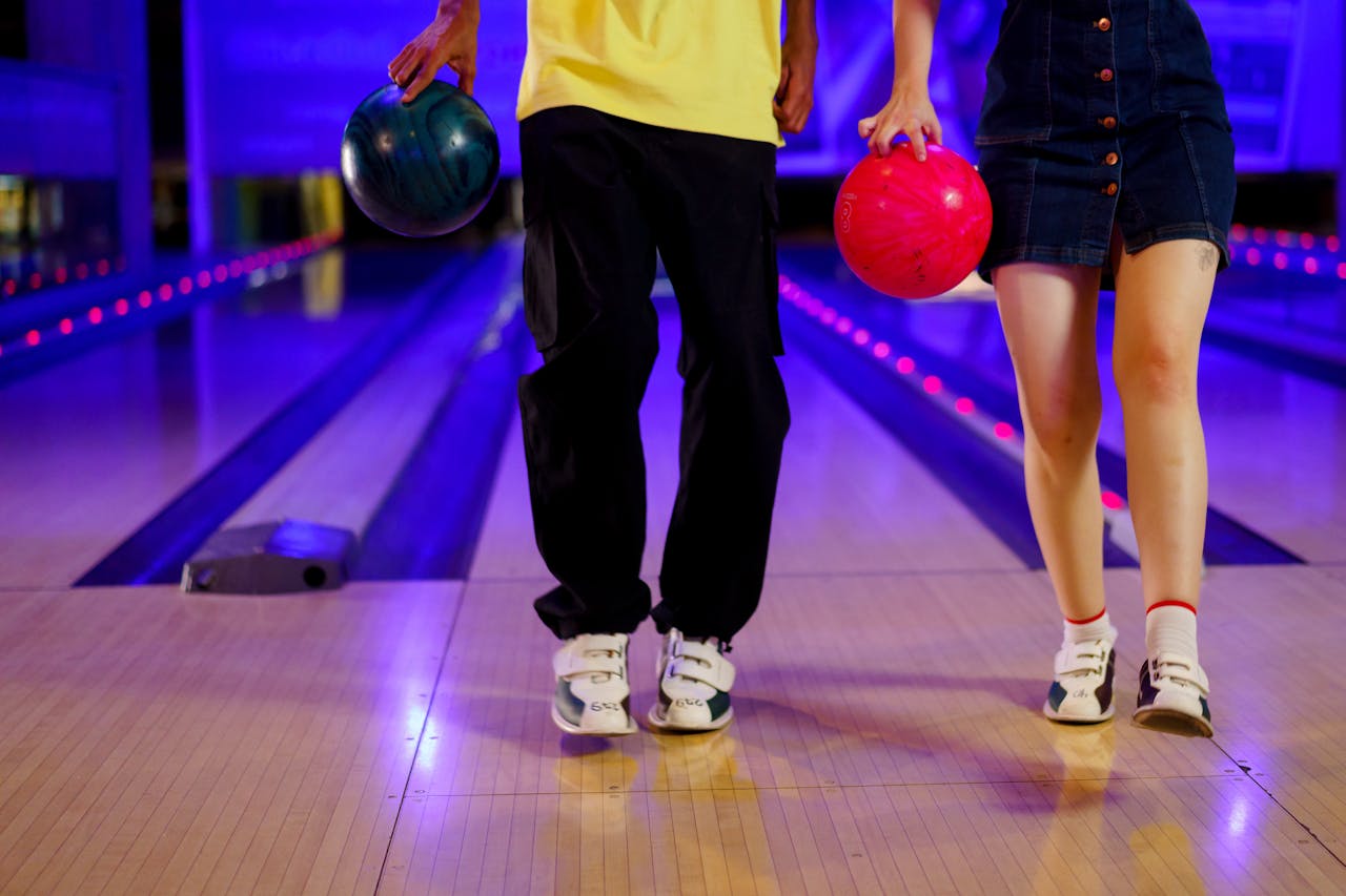 Close-up of two people walking together at a bowling alley, showing them both holding bowling balls and wearing bowling shoes